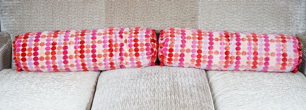 Two bolster cushions with brightly coloured cut velvet polka-dots. 90cm wide.