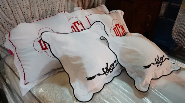 A set of four white pillows with red trim and initials 'DMC' to the centre, and two other white pillows with black trim, each approximately 55 x 55cm