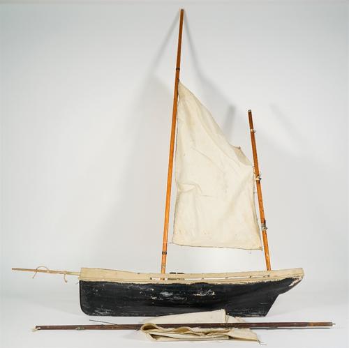 A small pond yacht, English, 20th century with single main mast, linen sails and black/white painted wooden hull, 64cm wide.