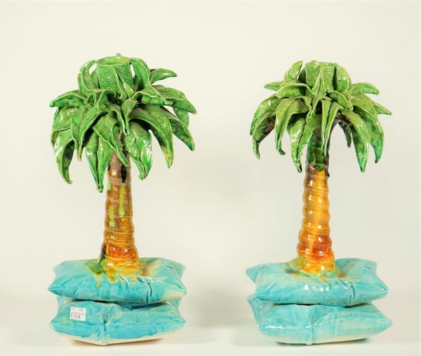 A pair of Katharine Morling pottery candlesticks, each modelled as a palm tree atop two blue cushions, signed to the base, 33cm high, (2). ARR