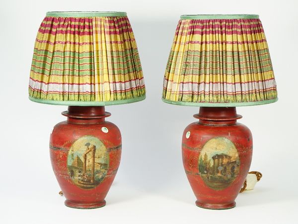 A pair of tole peinte table lamps, early 20th century, detailed with figures in a landscape against a deep red ground, with coloured shades, 52cm high