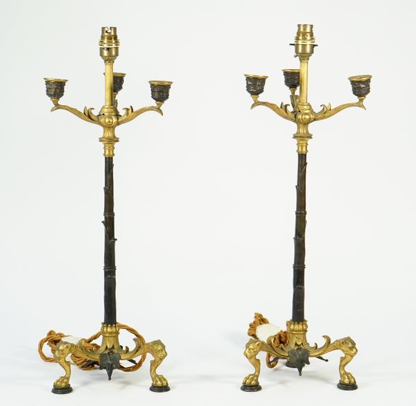 A pair of Regency style gilt and patinated three branch candelabra, converted to table lamps, each leaf cast column issuing three arms over a tri-form