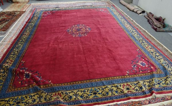 A Chinese carpet, the plain madder field with a central floral medallion, complementary sprandrels and a fawn lotus flower and vine border, 478cm x 35