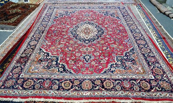 A Mashhed carpet, Persian, a madder field with a bold medallion and matching sprandrels, all with floral vines; an indigo palmette and vine border, 39