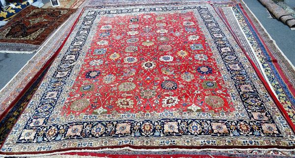 A Tabriz carpet, Persian, the madder field with an allover palmette, flower and vine design, an indigo complementary border, signed, 407cm x 300cm.