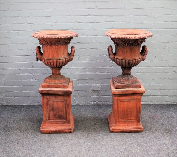 A pair of terracotta urns, with egg and dart rims and twin handles, on stepped square bases, 46cm diameter x 102cm high.