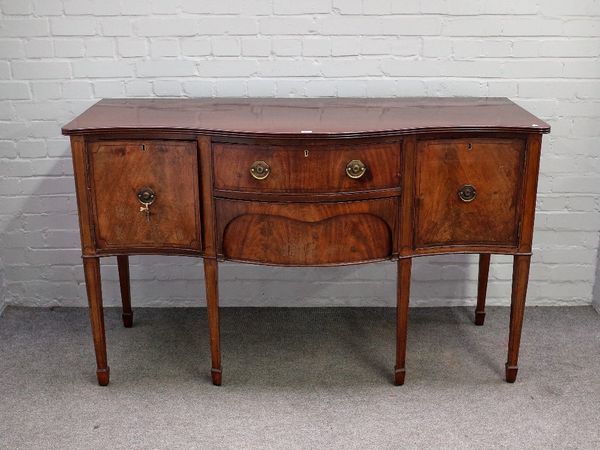 A George III inlaid mahogany sideboard, the serpentine top over a pair of central drawers, flanked by cupboards, on tapering square supports, 152cm wi