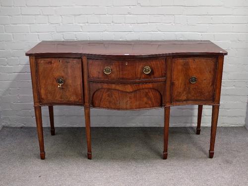 A George III inlaid mahogany sideboard, the serpentine top over a pair of central drawers, flanked by cupboards, on tapering square supports, 152cm wi