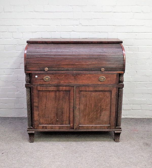 A George III mahogany tambour front writing desk, the lockable pull out fitted interior over a pair of panelled cupboards, flanked by spiral fluted co