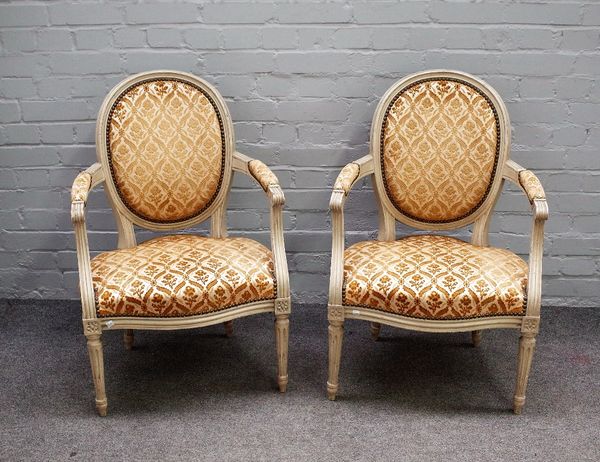 A pair of grey painted Louis XVI style open armchairs with serpentine seats on fluted supports, 57cm wide x 87cm high.