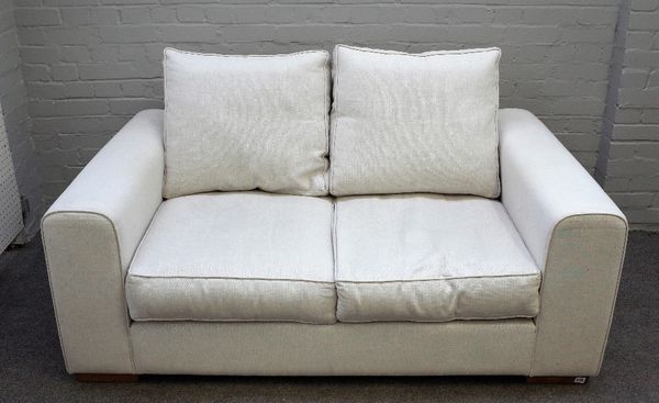 Heals; a Moretta small seat sofa upholstered in cream fabric on block feet, 163cm wide x 75cm high.