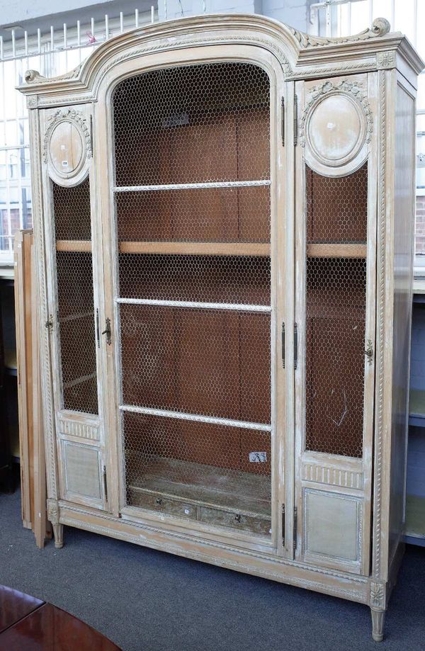 A French 19th century and later distressed painted beech display cabinet, the bonnet top over three chicken wire doors on squat tapering fluted suppor