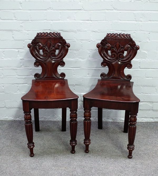 A pair of early Victorian mahogany hall chairs, with carved backs and solid bow seats on reeded supports, 39cm wide x 84cm high, (2).