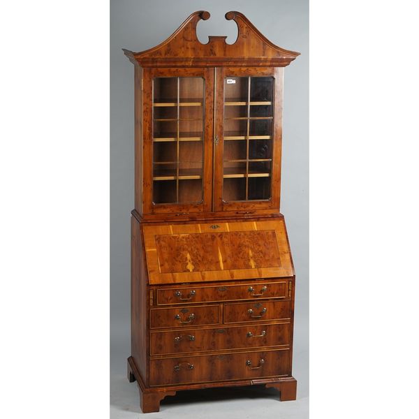 An early 18th century style yew bureau bookcase, the broken swan neck cornice over a pair of glazed doors and candle slides, the fitted stepped interi