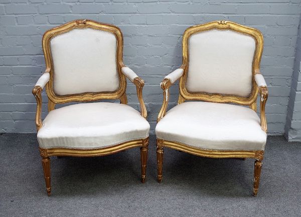 C Chevigny; a pair of Louis XVI gilt framed open armchairs, with serpentine seats, on tapering fluted supports, 70cm wide x 98cm high, (2).