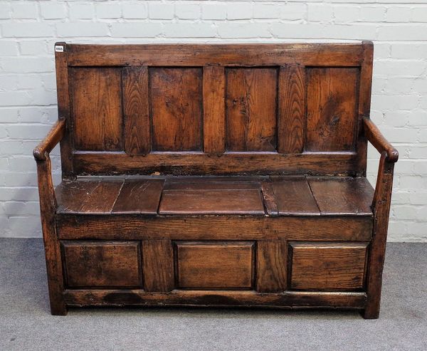 An 18th century oak box seat settle, the four panel back over open arms and lift seat on block feet, 130cm wide x 99cm high.