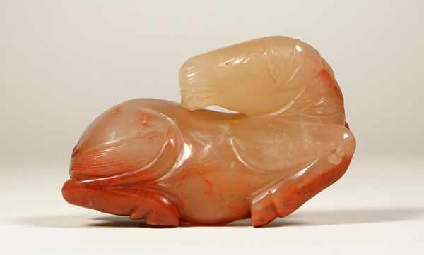 A Chinese agate figure of a horse, late 19th/20th century, the recumbent animal carved with head turned over its back, the stone of reddish-brown and