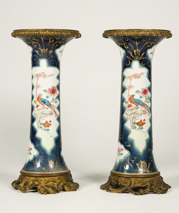 A pair of famille-rose blue ground gilt-metal mounted beaker vases, 19th/20th century, of slender form, painted with panels of birds and flowers insid