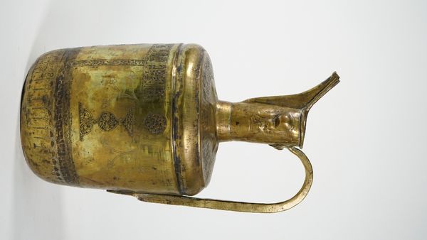 A Khorassan type brass ewer. modern, of cylindrical form with loop handle, the body engraved with a winged animal beneath script, 32.5cm. high.