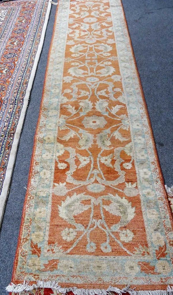 A Turkish runner, the burnt orange field with single rosettes, acanthus leaves and trailing vines; a pale indigo border, 390cm x 79cm.  B3