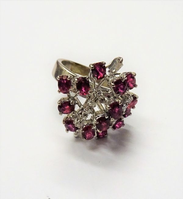 A ruby and diamond ring, in a pierced abstract design, mounted with mostly oval cut rubies, two rows of small circular cut diamonds and with two key s