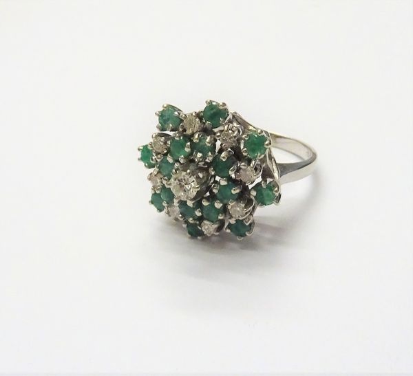 A white gold, diamond and emerald cluster ring, claw set with the principal circular cut diamond in a raised design at the centre and otherwise set wi