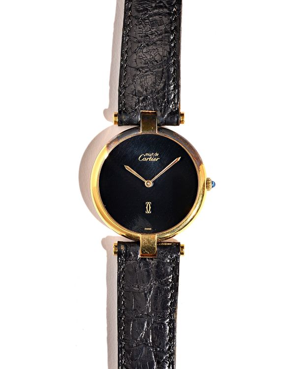 A Cartier Paris Quartz silver gilt circular cased wristwatch, the signed circular black dial with gilt hands, on a black leather strap, detailed to th