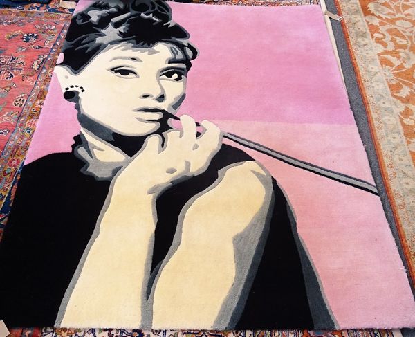 A machine made rug, the pink field depicting Audrey Hepburn, smoking a cigarette in a long holder, in black, grey and white, 200cm x 154cm.  C5