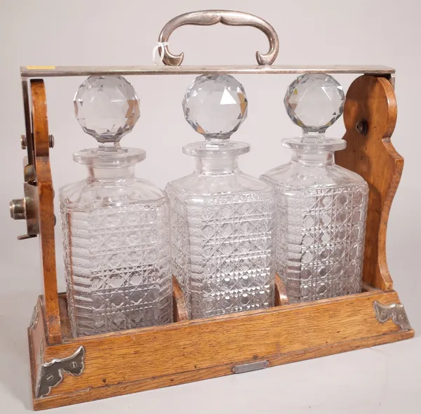 An early 20th century oak and silver plated mounted three division tantalus, with cut glass decanters, 35cm wide x 33cm high.  B1