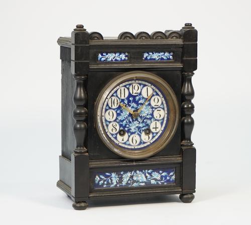 A Liberty style Arts & Crafts mantel clock, the ebonised case with inset foliate painted porcelain dial and plaques enclosing a two train movement wit