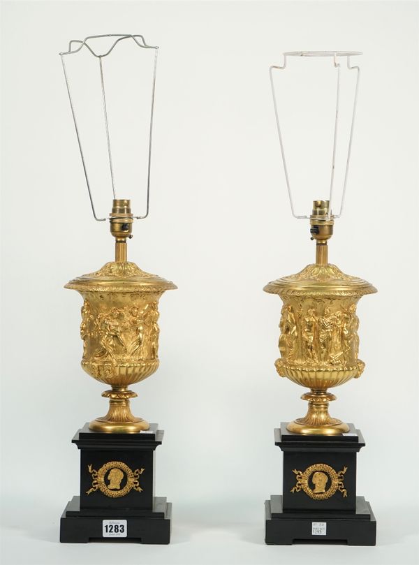 A pair of 19th century style gilt metal urns on back marble bases, converted to table lamps, the urns relief cast with classical figures over stepped