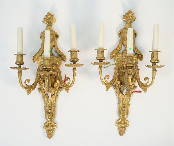 A pair of Empire style ormolu three light wall appliques, 20th century, each with flaming urn finials and acanthus cast backplate, 49cm high, (2).