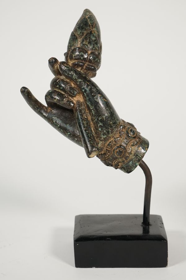 A patinated metal hand, cast holding a flower, probably Indian, 19th century, on an ebonised wooden plinth, 24.5cm high.