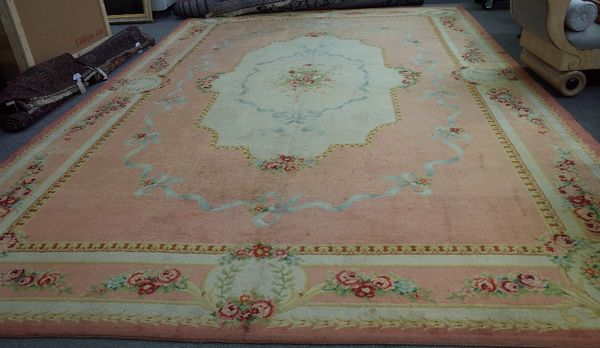 A Savonnerie carpet, French, the salmon pink field with a central ivory lozenge, ribbon and floral bouquet, outter ribbon design, a complementary rose