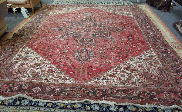 A Heriz carpet, Persian, the washed madder field with a bold angular medallion, ivory spandrels, all with angular vines, a black palmette and flower v