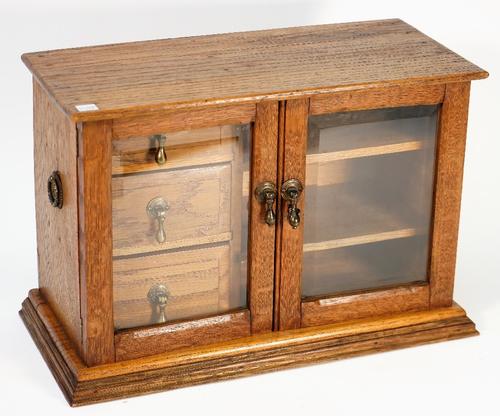 An early 20th century oak table top collector's chest the glazed door enclosing three drawers and shelves, 43cm wide x 29cm high.