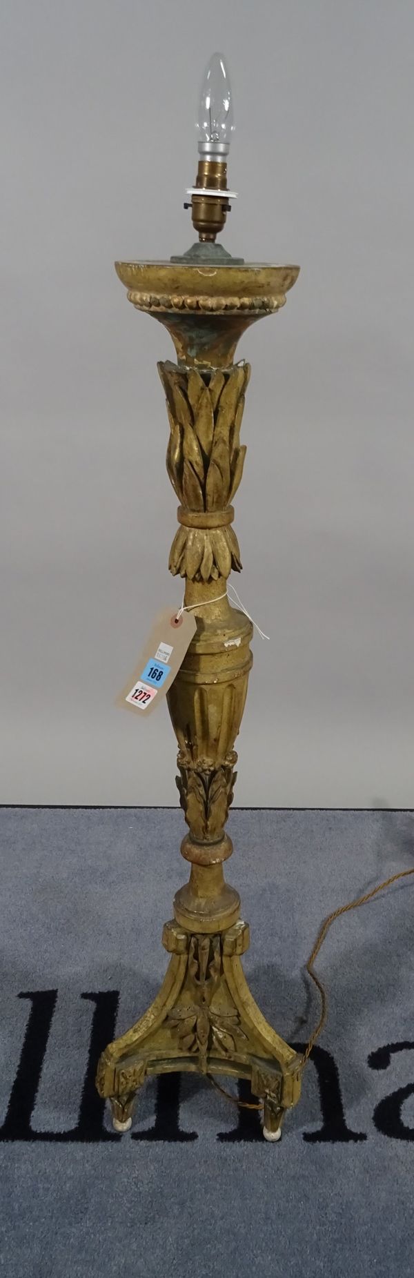 An 18th century giltwood altar candlestick (converted into a table lamp), carved foliate detail, distressed with old paint traces on a triform base, w