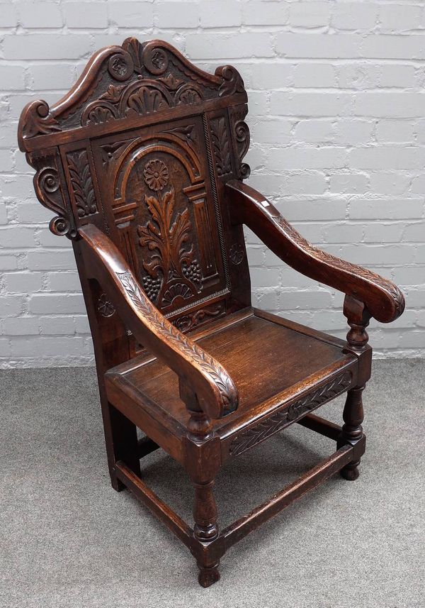 A Charles II style oak wainscot open armchair with carved panel back on baluster turned supports united by perimeter stretcher, 59cm wide x 108cm high