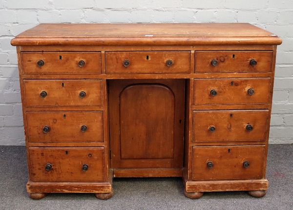 A Victorian pine kneehole writing desk, with nine drawers about the cupboard, on bun feet, 112cm wide x 77cm high.