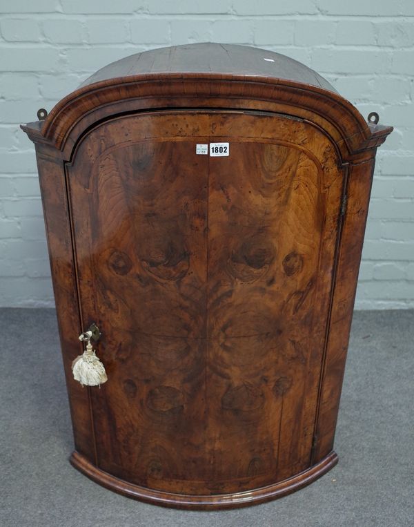 A mid-18th century figured walnut bowfront hanging corner cupboard, with bonnet top over single door, 70cm wide x 97cm high.