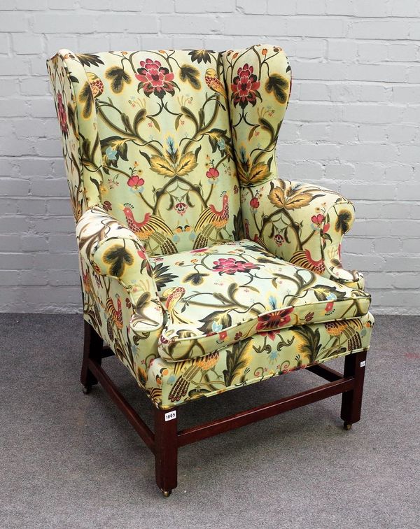 An 18th century wingback armchair, on mahogany block supports, united by stretchers, 90cm wide x 112cm high.