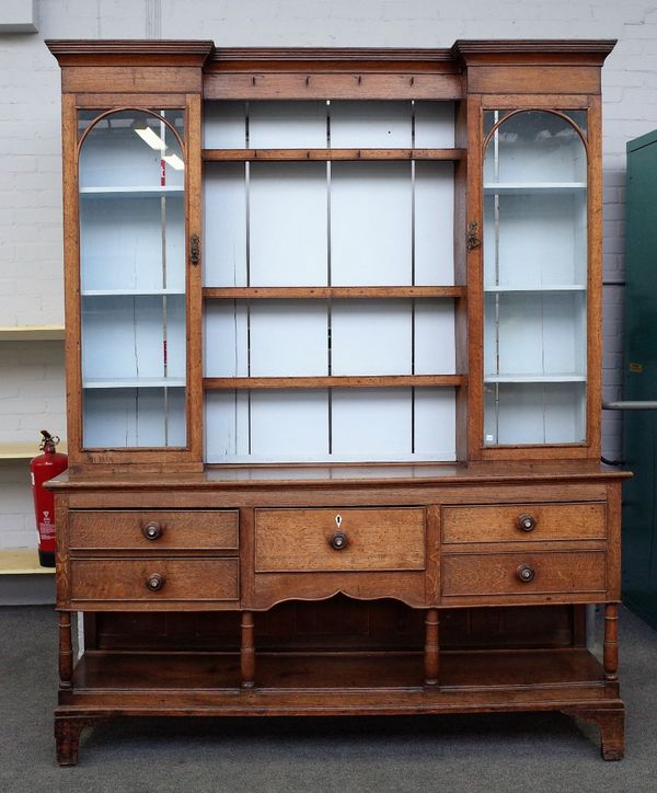 An 18th century and later oak dresser, the enclosed three tier plate rack flanked by glazed cupboards, the base with five frieze drawers on turned sup