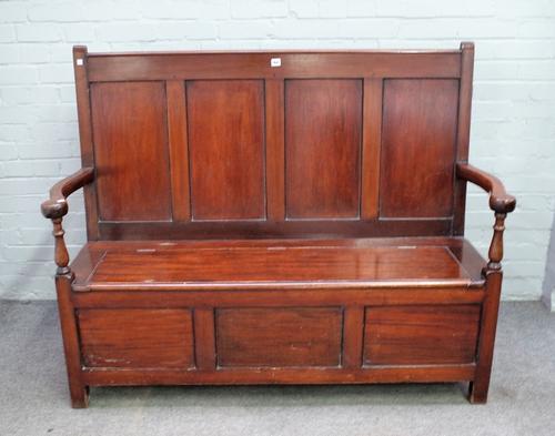 An Arts & Crafts mahogany box seat settle, the four panelled back over open arms, the lift seat over triple panelled front, 148cm wide x 114cm high.
