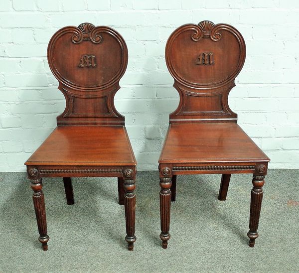 In the manner of Gillows; a pair of early 19th century mahogany hall chairs, with shell crest and shaped backs, on tapering reeded supports, 44cm wide