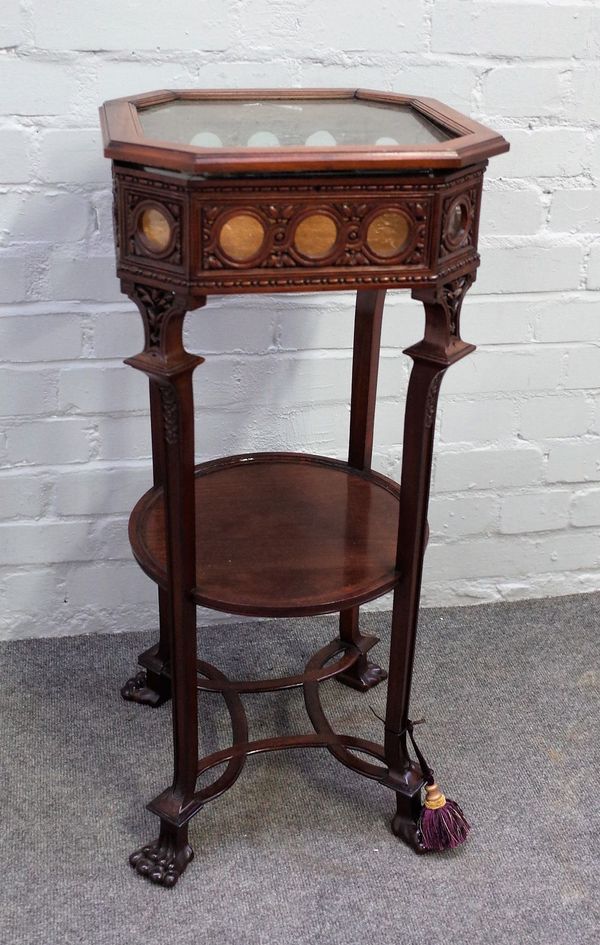 A late 19th century mahogany vitrine table with lift glazed octagonal top and sides on four square supports and paw feet, united by circular undertier