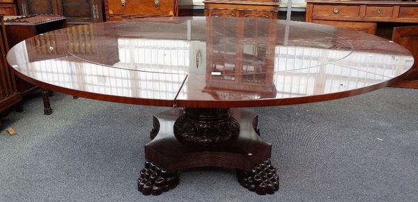 A modern mahogany extending 'Jupe style' dining table, the circular top 150cm diameter, with eight halo leaves, extending to 200cm diameter, raised on