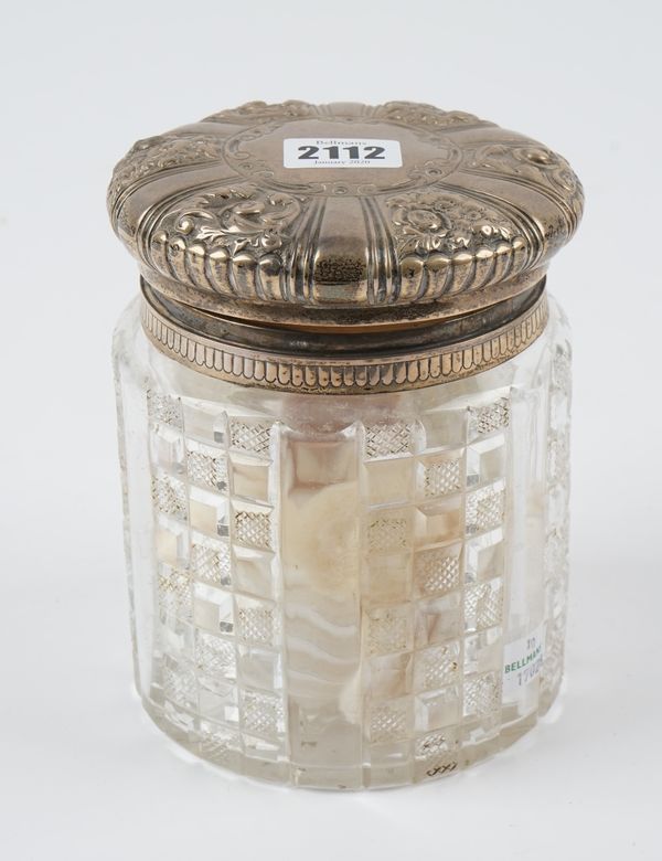 A late Victorian silver hinge lidded faceted glass cotton wool or toilet jar, the body with faceted and fluted decoration, the hinged cover with flora