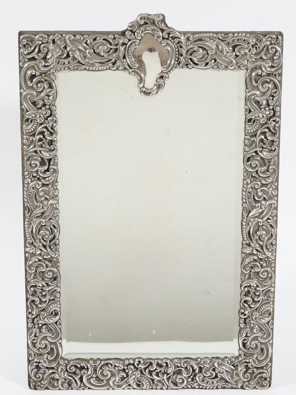 A silver mounted shaped rectangular strut backed mirror, fitted with a bevelled mirror glass, the wide border embossed and pierced with foliate scroll