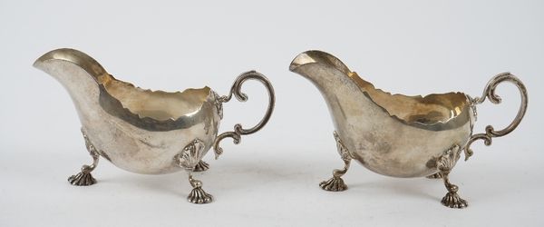 Two similar silver sauceboats, each having a scrolled handle, a shaped rim and raised on three shell capped feet, Birmingham 1928 and 1929, combined w