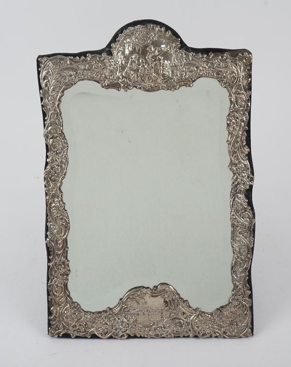 A silver mounted shaped rectangular strut backed mirror, the shaped border with embossed decoration and fitted with a bevelled edge glass, modern, siz